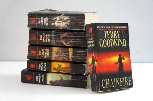 A stack of five paperback books of Terry Goodkind's 'Good Kindness' series, with the book 'Chainfire' standing upright next to the stack on a white surface against a light gray background.