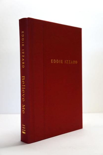 A hardcover book titled 'Eddie Izzard Believe Me' with a textured dark red cover and gold lettering, standing upright on a white surface against a white background.