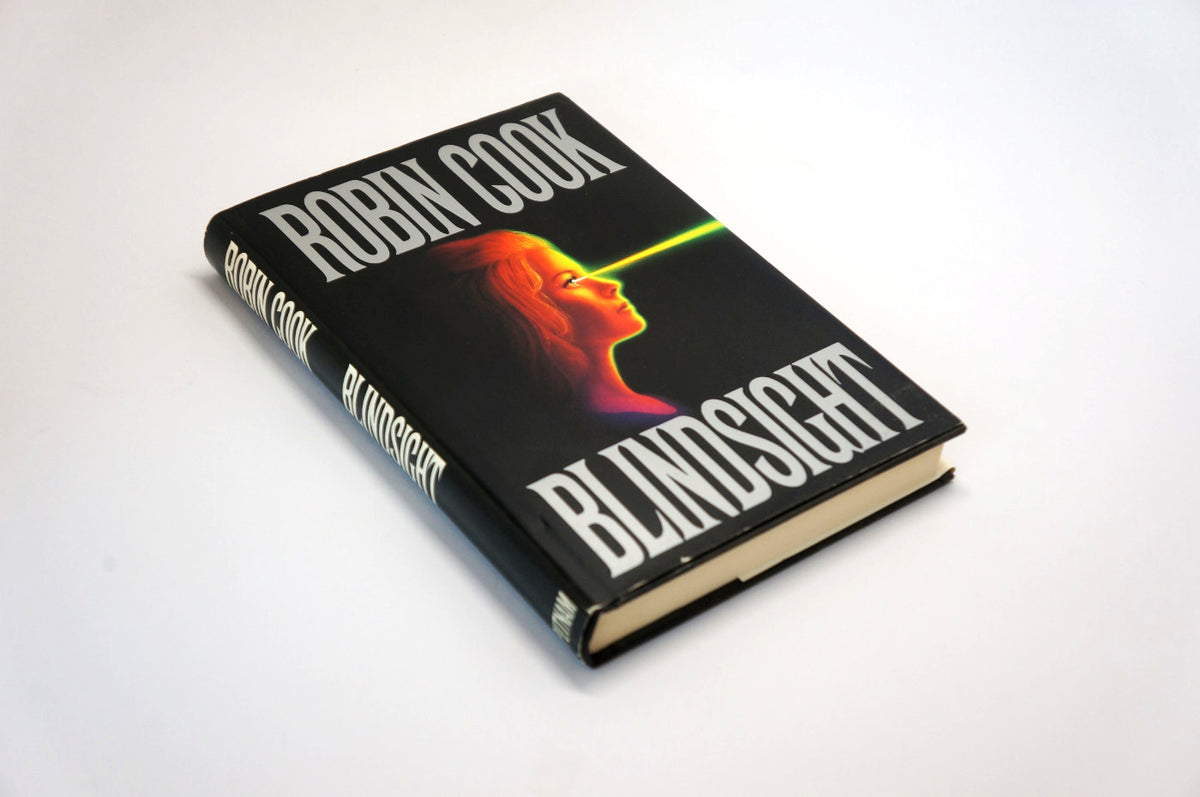 A hardcover book titled 'Blindsight' by Robin Cook, featuring a black cover with a stylized illustration of a woman's profile and a bright green laser beam, photographed on a plain white background.