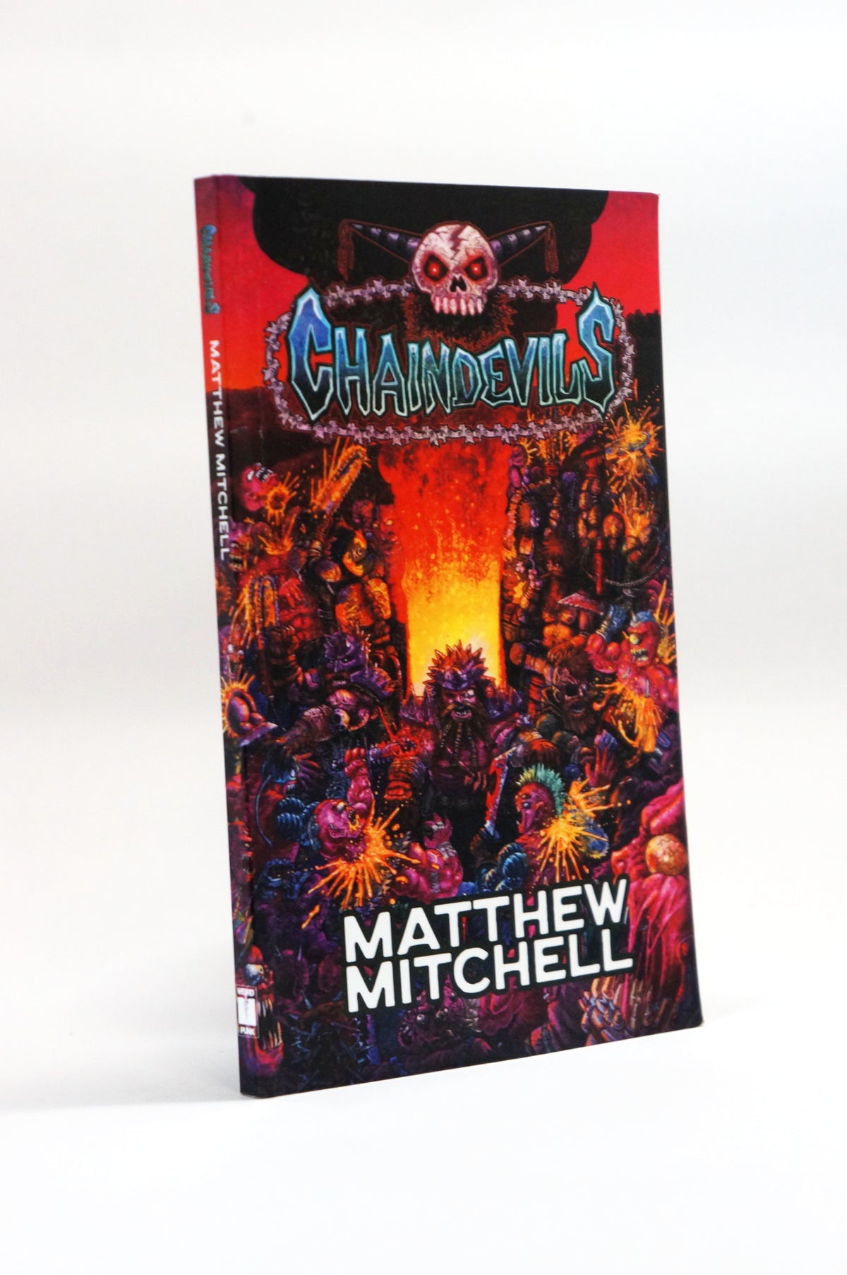 The book cover of 'Chainsawdevils' by Matthew Mitchell, featuring a highly detailed, colorful fantasy illustration of demonic creatures in a fiery red and orange landscape, shown standing upright on a white background.