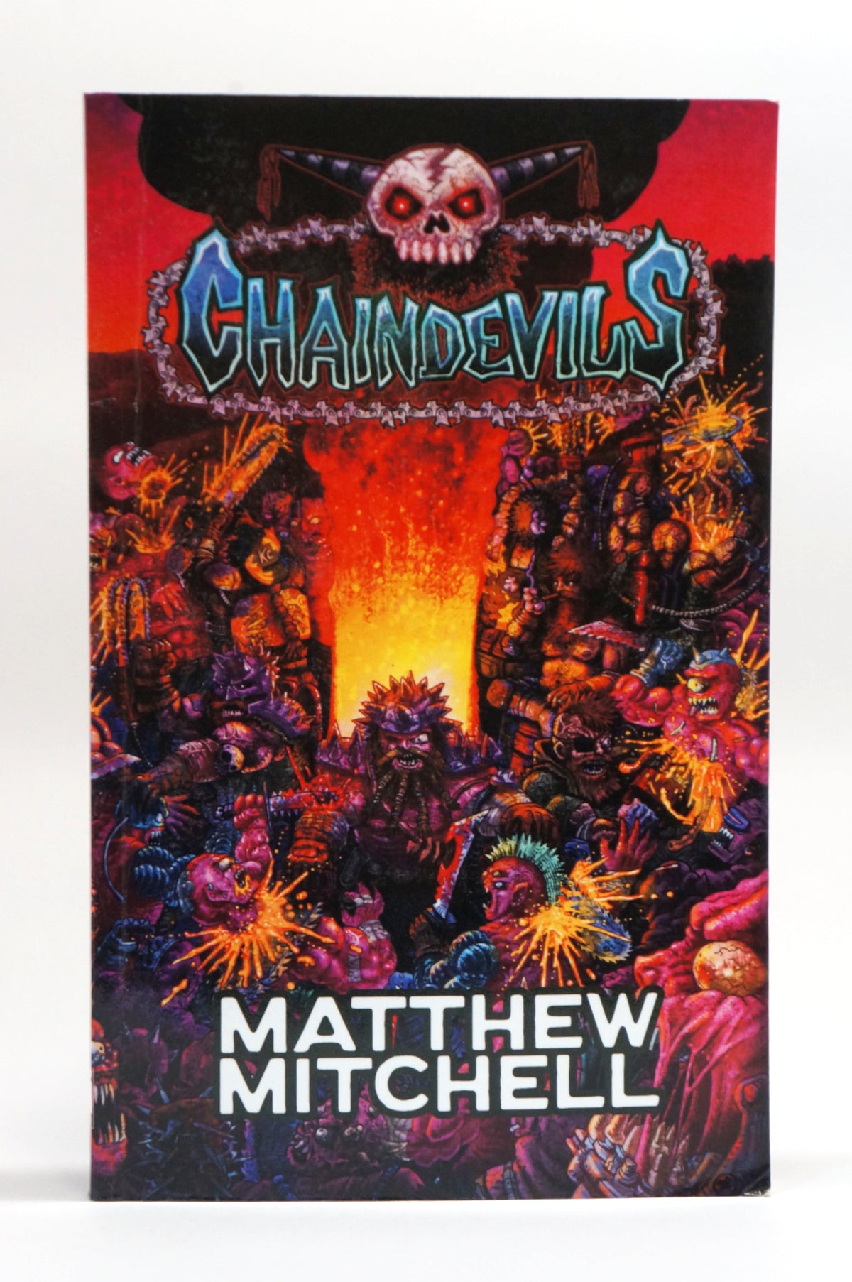 The book cover of 'Chainsawdevils' by Matthew Mitchell, featuring a highly detailed, colorful illustration of demonic creatures surrounding a glowing lava fissure, set against a plain white background.