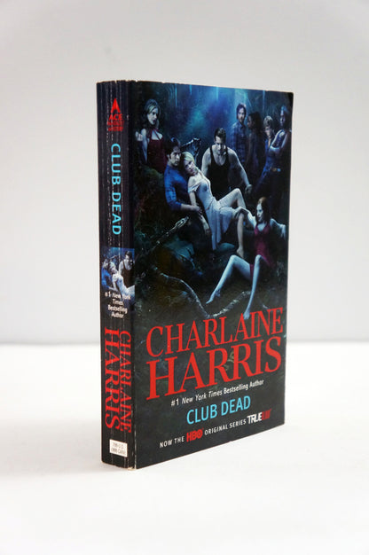 A paperback titled 'Club Dead' by Charlaine Harris, standing upright against a plain light background. The cover and spine feature dark blue and black artwork with red and white text.