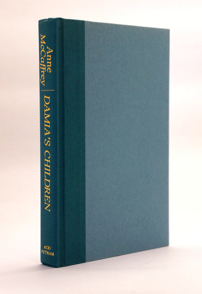 A hardcover book titled 'DAMIA'S CHILDREN' by Anne McCaffrey, standing upright at a slight angle. The book features a dark teal-green spine with gold lettering and a matching dark teal-green front cover, set against a plain off-white background.