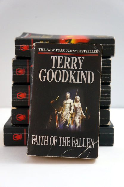 A vintage paperback copy of Terry Goodkind's 'Faith of the Fallen' book, standing upright in front of a stack of identical books on a white surface against a white background.