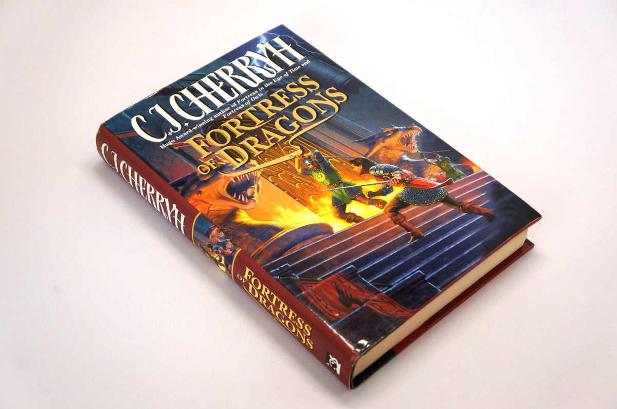A hardcover book titled 'Fortress of Dragons' by C.J. Cherryh, photographed at an angle on a plain white background.