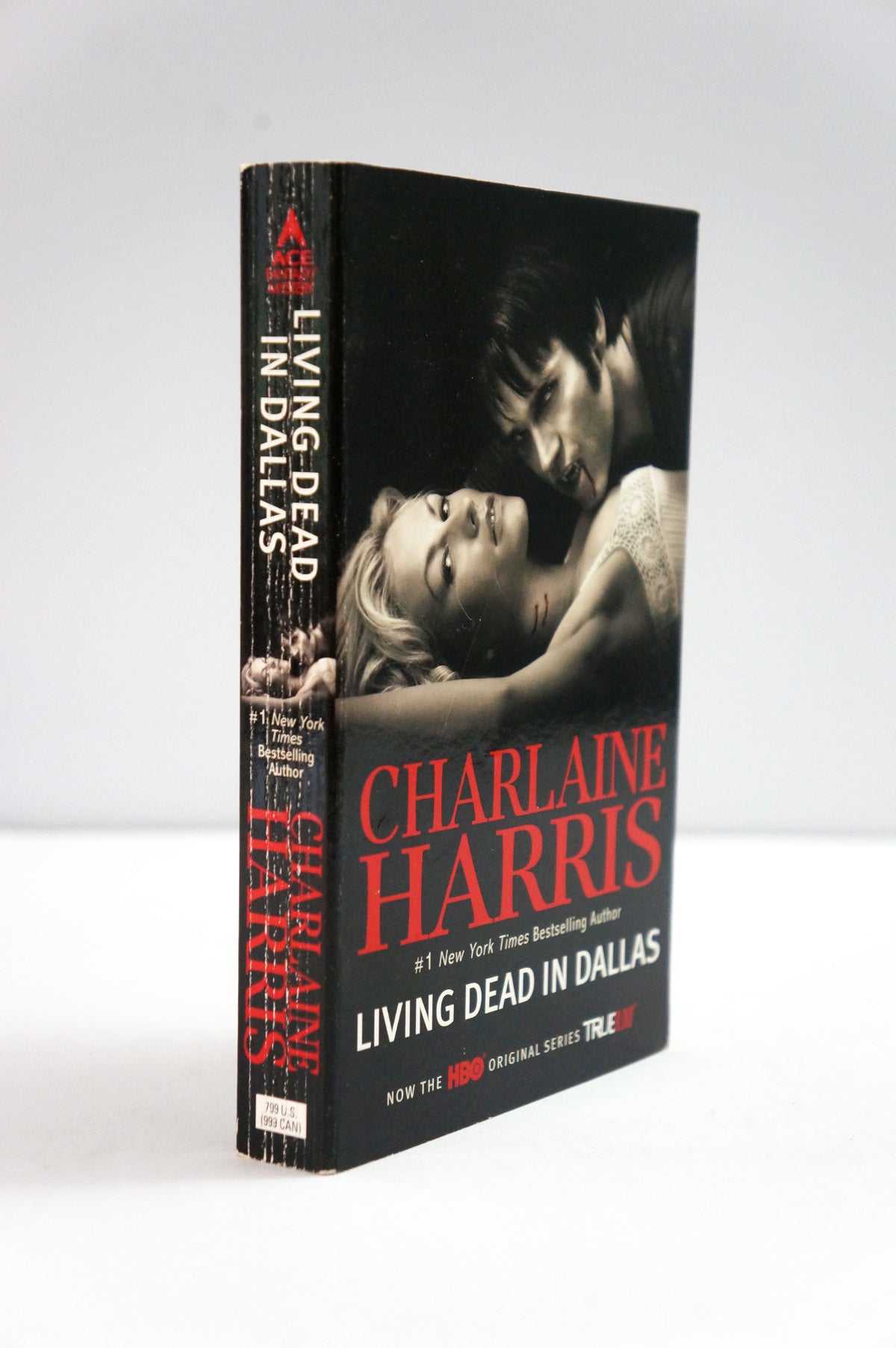 A paperback of Charlaine Harris's 'Living Dead in Dallas' standing upright at a slight angle. The cover is predominantly black with a dramatic black-and-white photo of a couple and bold red title text.