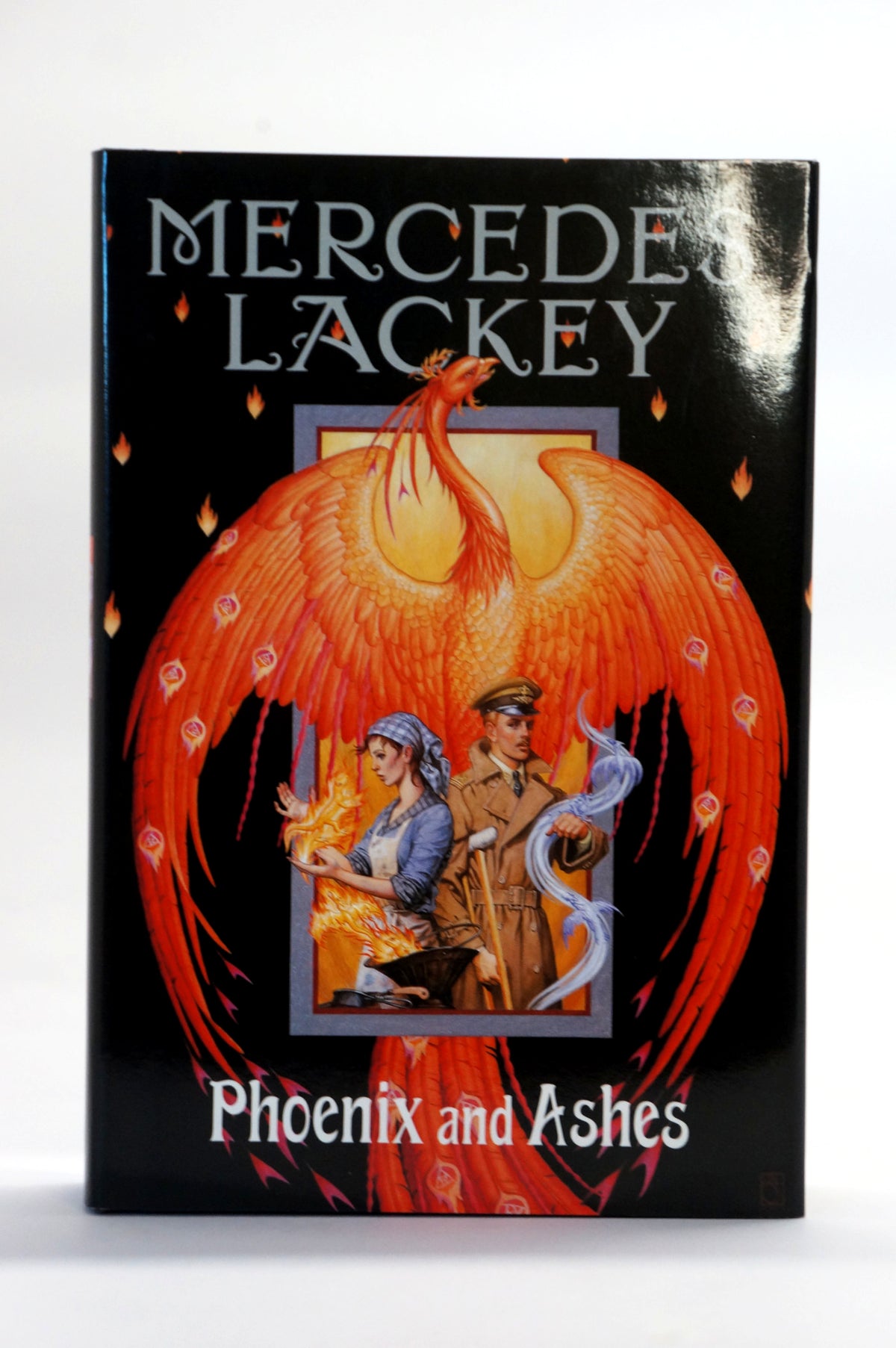 Mercedes Lackey's book 'Phoenix and Ashes' featuring a black cover with a large orange-red phoenix illustration and two small illustrated figures in a central panel.