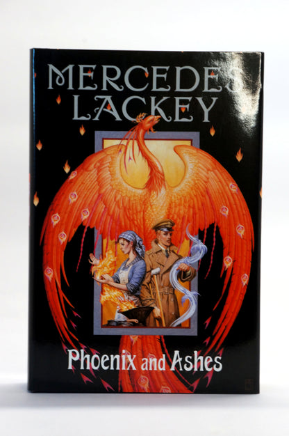 Mercedes Lackey's book 'Phoenix and Ashes' featuring a black cover with a large orange-red phoenix illustration and two small illustrated figures in a central panel.