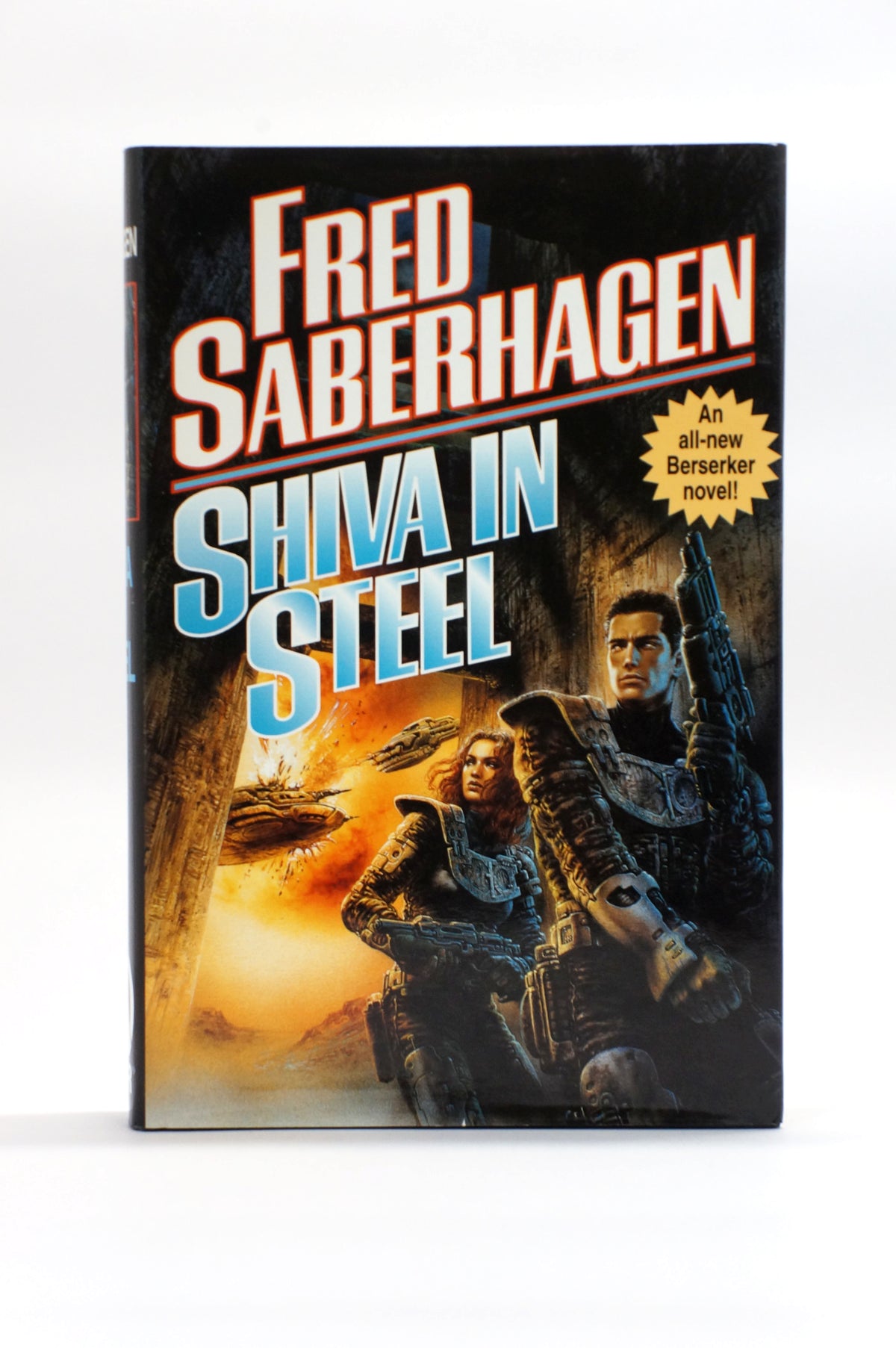 A vintage hardcover book of Fred Saberhagen's 'Shiva in Steel' standing upright against a white background. The cover features a dramatic sci-fi illustration with two soldiers in armor, a spaceship, and a bright orange explosion, with the title in large blue and white lettering.