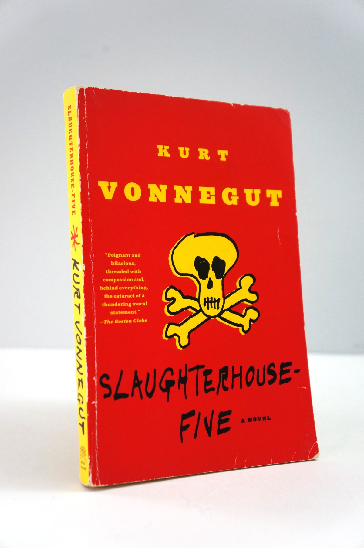 Book cover of 'Slaughterhouse-Five' by Kurt Vonnegut with a red background and yellow skull and crossbones design.