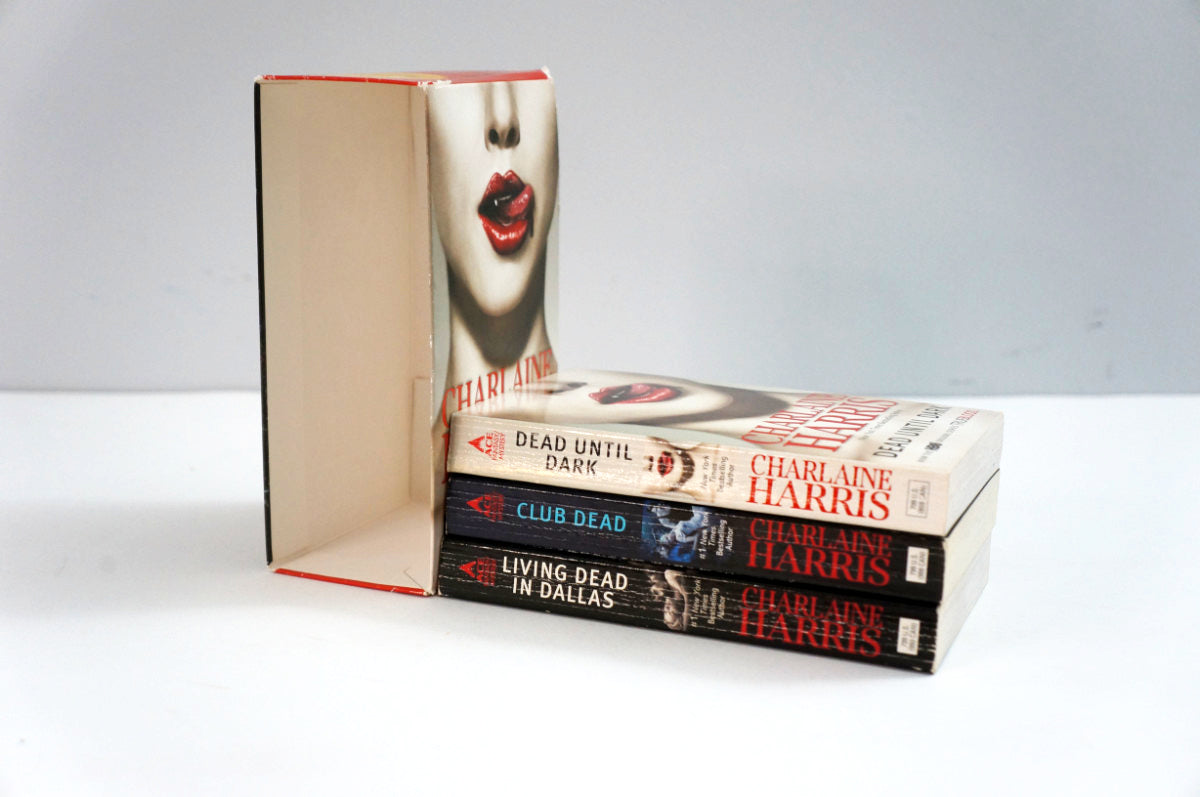 Three books by Charlaine Harris stacked on a white surface with the slipcase standing upright behind them. 
