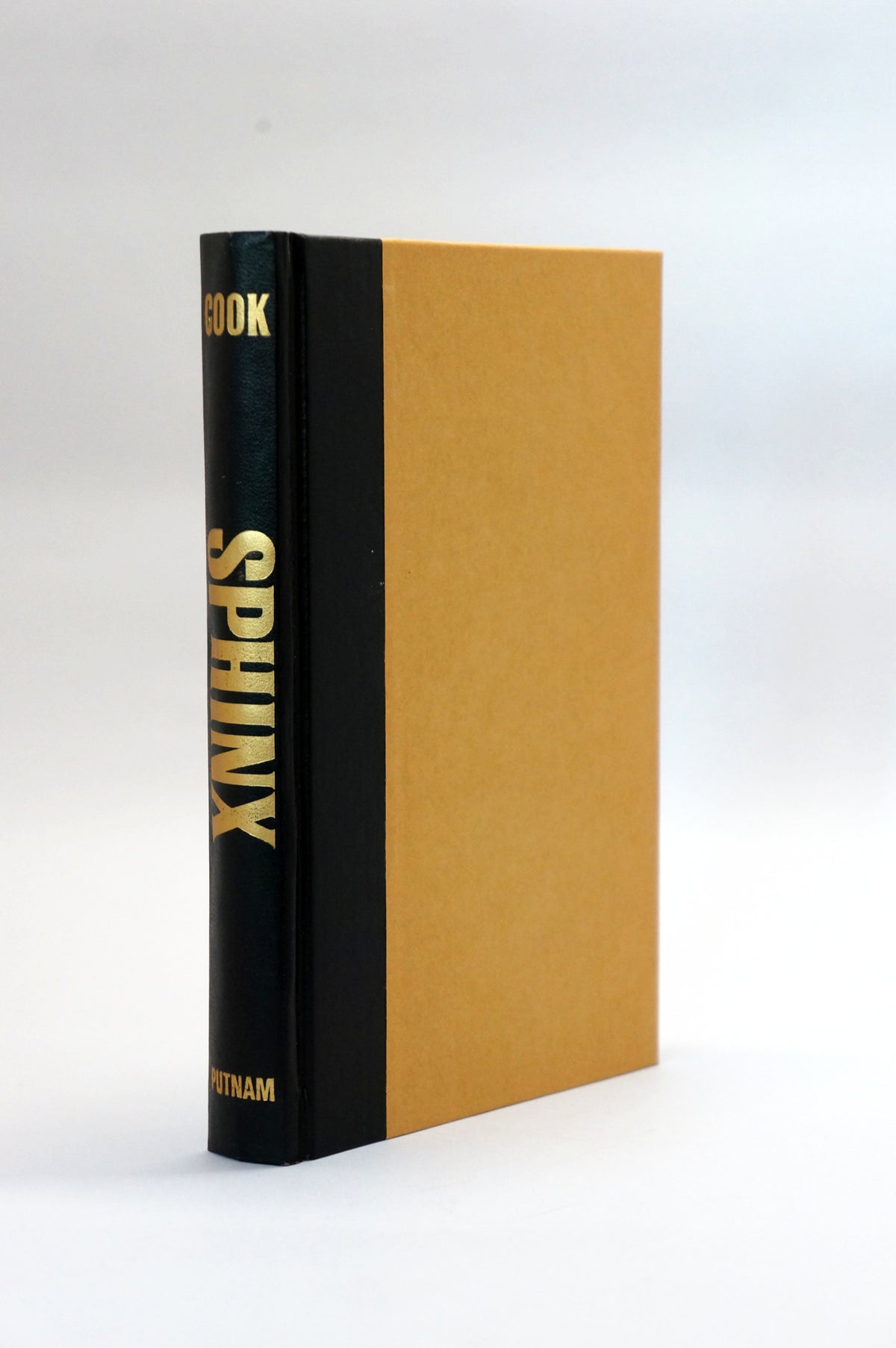 A hardcover book titled 'SPHINX' standing upright, featuring a black spine with gold lettering and a tan or ochre-colored front cover, photographed against a clean white background.