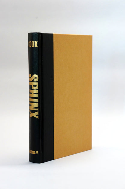 A hardcover book titled 'SPHINX' standing upright, featuring a black spine with gold lettering and a tan or ochre-colored front cover, photographed against a clean white background.