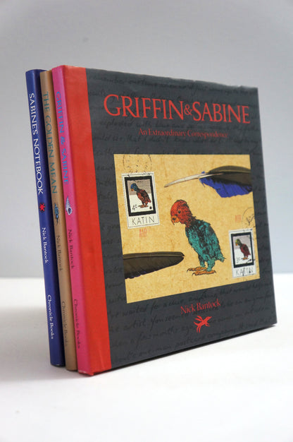 A set of three hardcover art books by Neil Darrell titled Griffin & Sabine, arranged in a fan-like stack. The front book is dark gray with red lettering and an illustration of a green parrot, while the spines show blue, pink, and red covers.