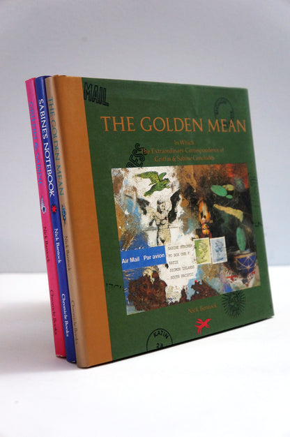 A set of three hardcover books standing upright, with the front book titled "The Golden Mean" in green cover art, and the spines showing "Sax's Notebook," "Camino de Santiago," and "The Golden Mean.".